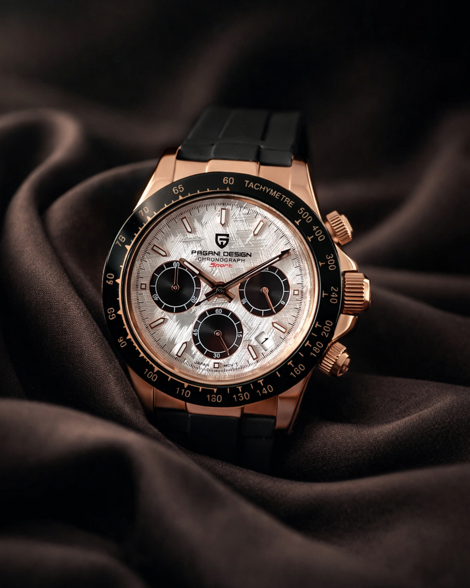Rose gold chronograph watch with black strap on dark fabric